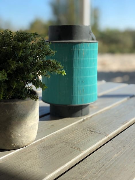 A close-up shot of a portable, ruggedized bluetooth speaker sitting on a patio table beside a pool in a sunny US backyard. The speaker is playing music, with a smartphone visible nearby. Focus on highlighting the speaker's durability and portability.