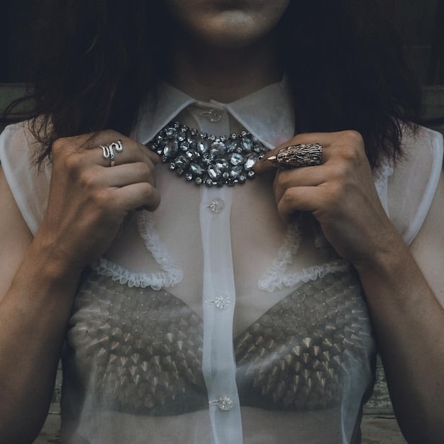 A close-up shot of a stylish woman's hands subtly adjusting the collar of a chic, affordable shein blouse, with delicate jewelry visible.