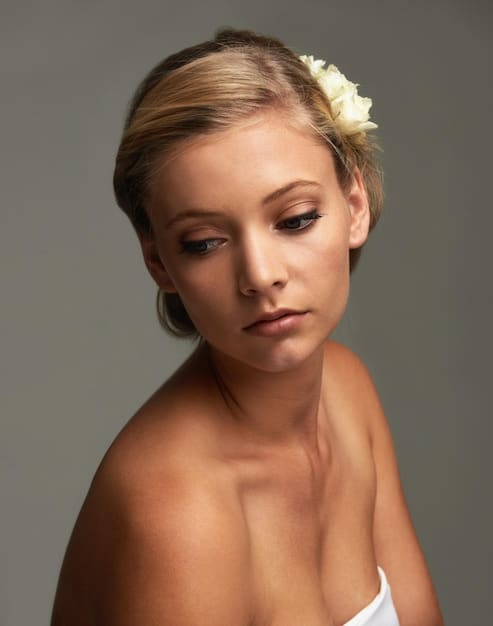 A detailed close-up shot of a woman's face, showcasing elegant, natural makeup and a beautifully styled, simple updo, perfect for a wedding guest.