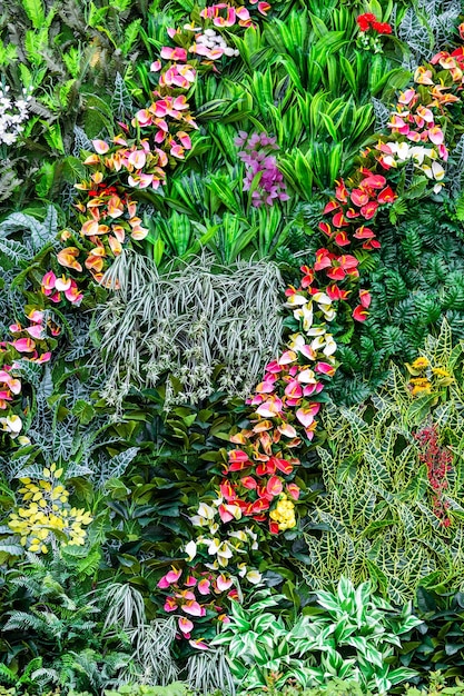 A vibrant vertical garden on a sunny backyard wall. A variety of colorful flowers, herbs, and leafy greens are planted in stacked containers and hanging baskets. The wall is made of reclaimed wood, adding a rustic touch to the modern design.