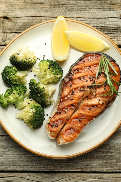 A perfectly grilled salmon fillet with a side of steamed broccoli and a lemon wedge on a white plate. The focus is on the flaky texture of the salmon and the vibrant green of the broccoli, highlighting a healthy and delicious meal option to Lower Your Cholesterol Naturally: 7 Foods to Add to Your Diet Starting Today.