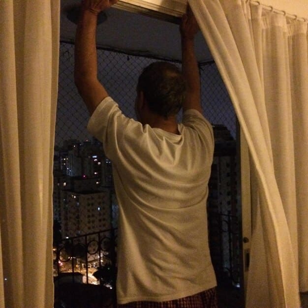 A person adjusting blackout curtains in a bedroom, showcasing the effort to minimize light exposure for a better sleep environment. The room is dark and cozy, emphasizing the importance of light control to improve sleep quality.
